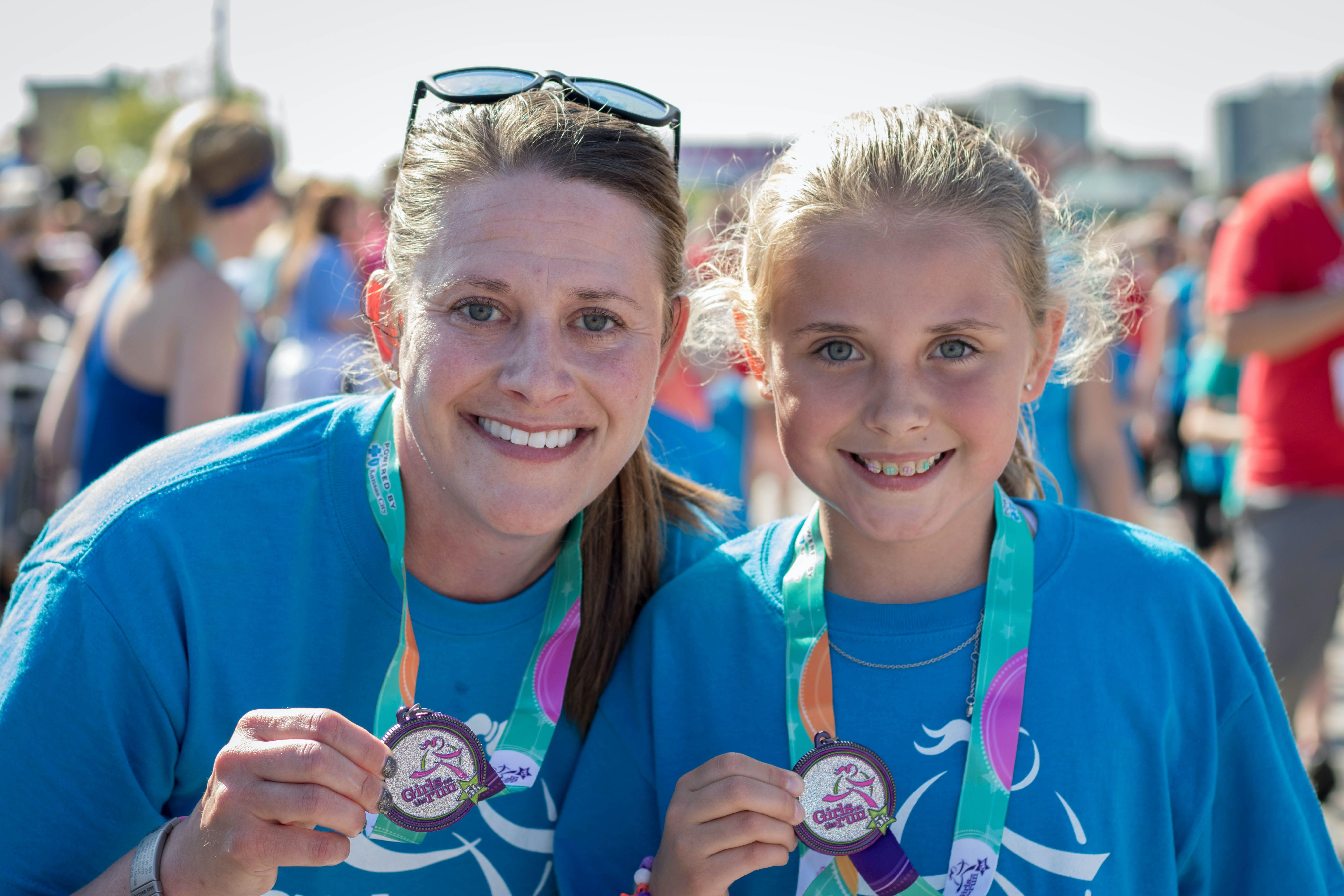 A Girls on the Run coach is wearing a green shirt and running with a program participant.